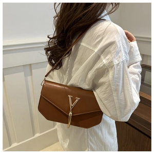 Brown leather crossbody bag with gold V emblem and tassel detail on a model side view