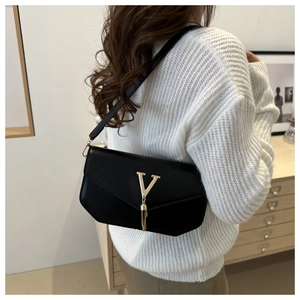Detail of a black envelope crossbody bag with a gold V-shaped tassel and leather strap