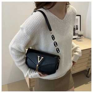 Elegant black square crossbody bag with gold V logo and tassel worn by a model