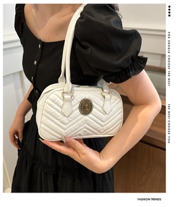 Close-up of white quilted tote bag featuring V-shaped stitching and vintage metal medallion