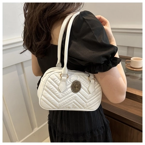 Close-up of white quilted handbag with chevron stitching and vintage bronze emblem
