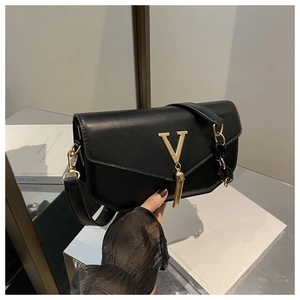 Detail of black crossbody bag featuring a golden V-shaped buckle and metal tassels