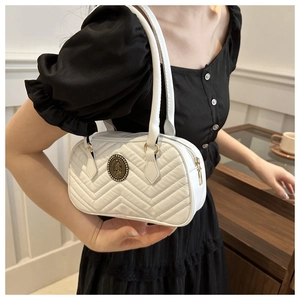 Close-up of white quilted handbag featuring a vintage metal emblem and V-shaped stitching
