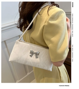 Detail of white textured underarm bag with silver bow buckle worn on woman's shoulder