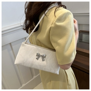 Detail of white underarm bag with silver bow ornament and rippled texture on model