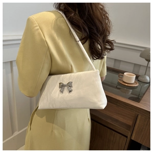 Detail of a creamy white satin bucket bag with silver butterfly knot on a model shoulder