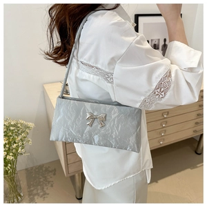Detail of silver-grey pleated baguette bag with metal bow buckle on a model shoulder