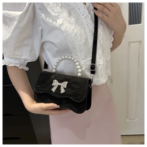 Detail of black wave-edged mini crossbody bag with pearl handle and silver bow accent