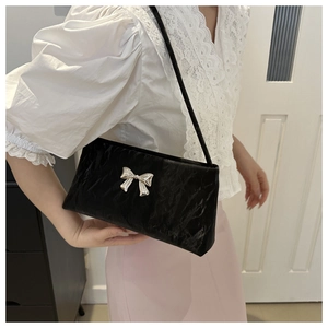 Detail of black underarm bag with pleated texture and silver metal bow decoration
