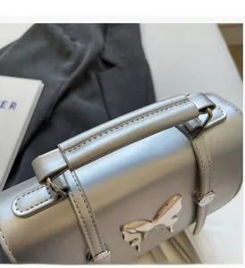 Detail of silver metallic tote bag featuring a 3D butterfly buckle and reinforced handle