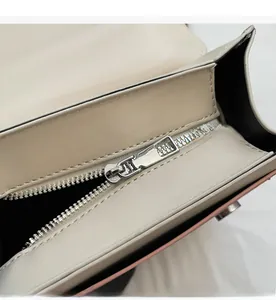 Close-up of a high-quality silver metal zipper on a beige matte textured crossbody bag
