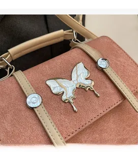 Macro detail of coral pink bag featuring silver butterfly metal ornament and matte texture