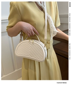 Detail of white half-moon crossbody bag with V-quilted texture and gold metal hardware