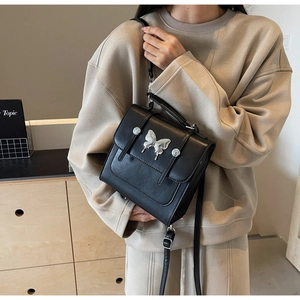 Detail of black square shoulder bag with silver butterfly charm and metal rivets