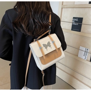 Model wearing a dual-tone backpack with metal butterfly clasp on a neutral background