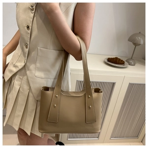 Detail of beige minimalist tote bag with gold rivets shown in a lifestyle setting
