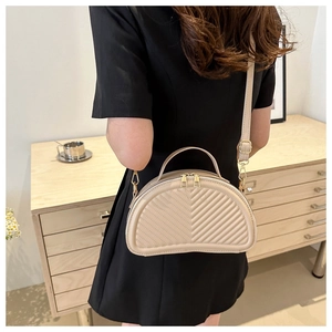 Beige crescent saddle bag with V-shaped quilting detail worn by a model in a cozy room