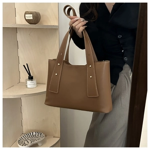 Detail of brown tote bag with white contrast stitching and gold rivets on leather