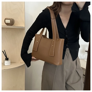 Brown leather tote bag featuring golden studs and long shoulder straps on a casual model