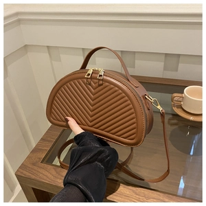 Detail of brown chevron quilted crescent handbag with gold zippers on a wooden table