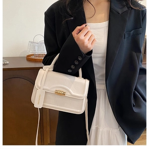 Detailed view of white leather crossbody bag with metal buckle and branded fashion tag