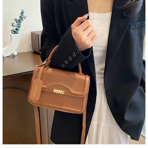 Detail of tan leather crossbody bag featuring gold metal lock and fashion tag accessory