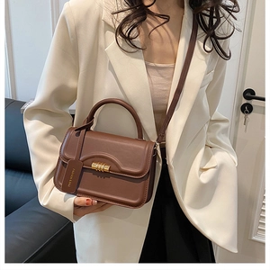 Detail of dark brown leather handbag with gold metal lock and elegant top handle on white suit