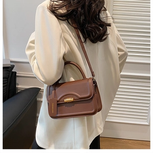 Brown matte leather crossbody bag with golden spiral lock shown on model from side angle