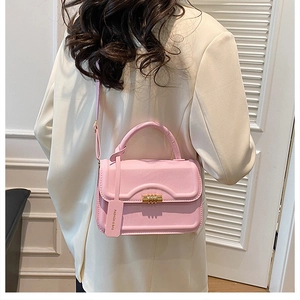 Pink synthetic leather crossbody bag with golden twist lock shown on a model's shoulder