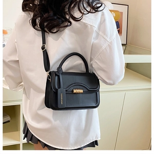 Black leather small square bag shown as a crossbody on a model in a casual indoor setting