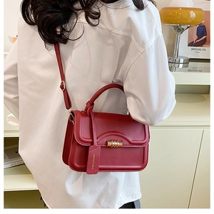 Detail shot of a red leather crossbody bag featuring a gold cylindrical twist-lock closure