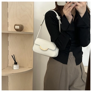 Détail d'un sac à bandoulière blanc avec boucle fer à cheval dorée et sangle nouée