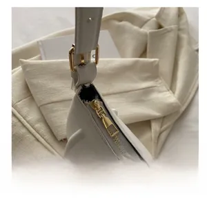 Detailed close-up of smooth gold metal zipper and adjustable strap buckle on a white bag