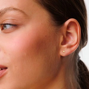 Close-up of golden four-prong stud earrings with clear zircon on ear lobe and conch