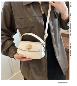 Detail of cream leather underarm bag with golden shell-shaped buckle and crossbody strap