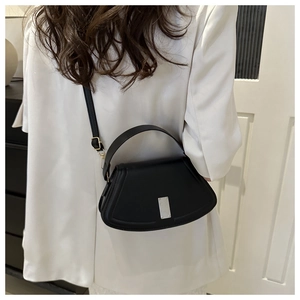 Elegant black saddle shoulder bag with silver buckle and top handle in a minimalist style