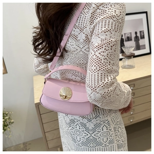 Pink crossbody bag with golden shell buckle detail shown in a cozy indoor setting