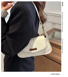 Close-up of a white leather baguette bag with a gold metal buckle on a dark suit