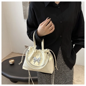 Détail du sac seau crème avec chaîne en perles et ornement de papillon argenté