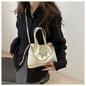 Détail du sac seau crème avec bijou papillon et bandoulière en perles élégante
