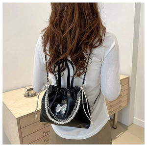 Détail du sac seau noir en PU avec breloque papillon argentée et chaîne de perles