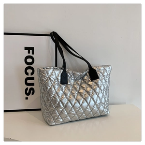 Detail of silver metallic quilted tote bag with black straps and geometric stitching