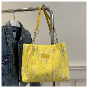Close-up of yellow tote bag featuring quilted texture and colorful wave embroidery