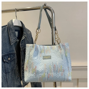 Close-up of light blue pleated tote bag with colorful embroidery and metal chain strap