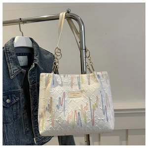 Detail of colorful striped embroidery and gold chain handle on white tote bag