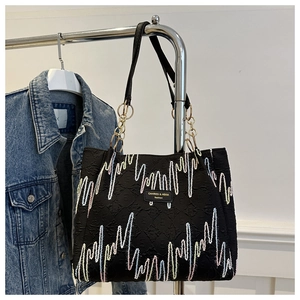 Detail of black textured tote bag with colorful wave embroidery and chain handle