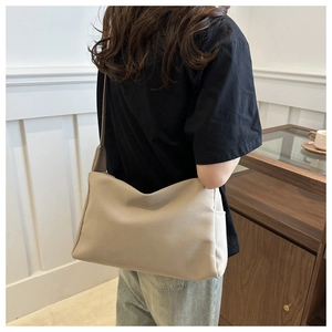 Model wearing a large beige nylon crossbody bag showing the drape and adjustable strap