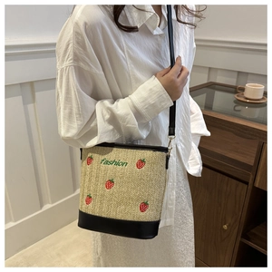 Detail of strawberry embroidery and black leather trim on a woven straw bucket bag