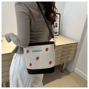 Detail of straw bucket bag featuring strawberry embroidery and black leather trim accents