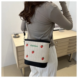 Detail of straw bucket bag featuring strawberry embroidery and black leather bottom